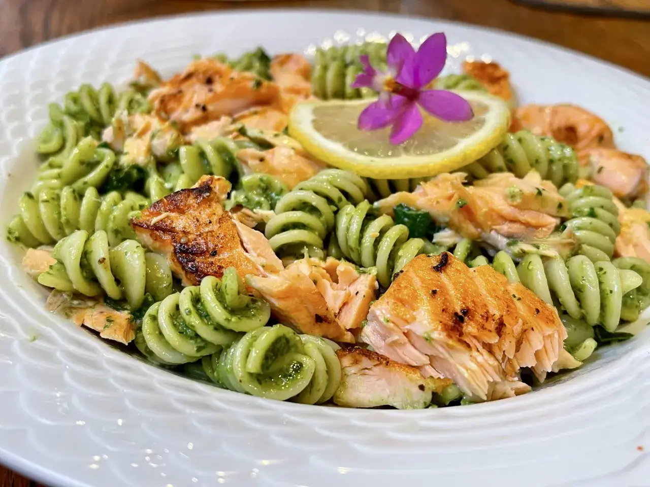 Fusilli z łososiem i aromatycznym pesto, udekorowane plasterkiem cytryny i fioletowym kwiatkiem.