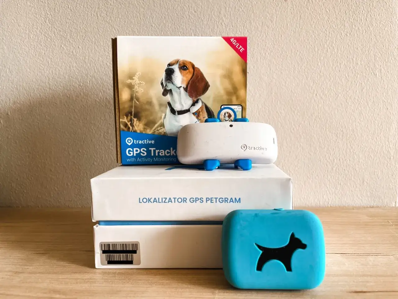 Zestaw Tractive: lokalizator GPS dla psa, jego opakowanie z wizerunkiem beagla i niebieski gadżet z sylwetką psa.