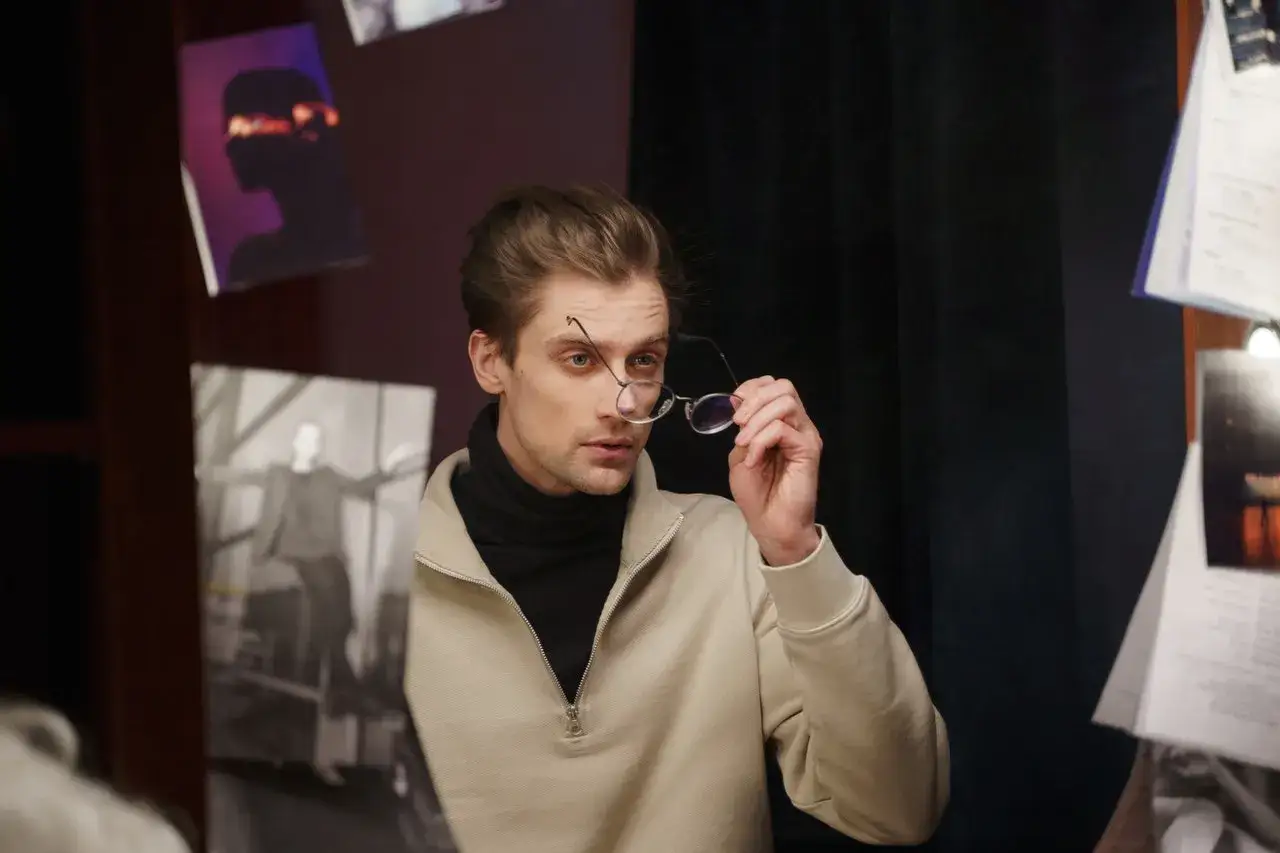 Młody mężczyzna w okularach, otoczony zdjęciami, zastanawia się, ile zarabia polski aktor.