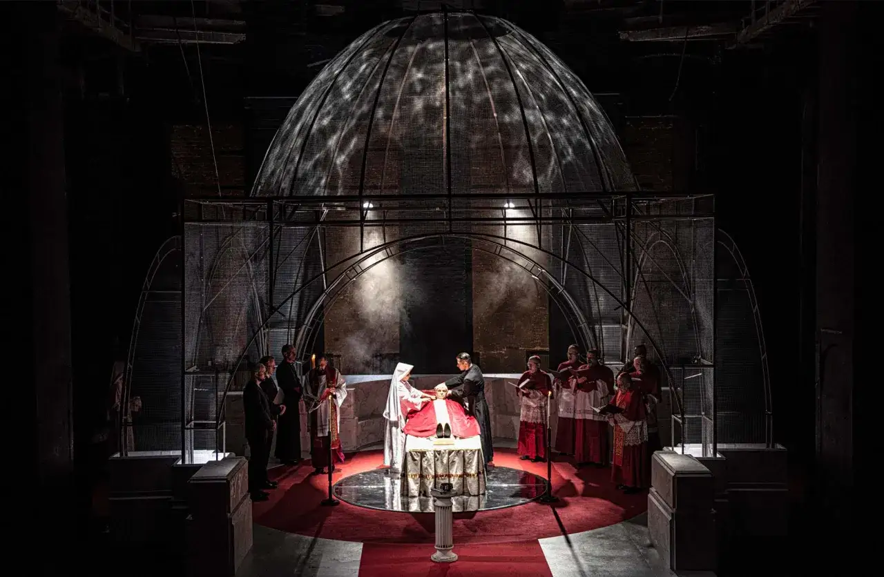 Scena teatralna z postaciami w strojach duchownych pod kopułą. Zastanawiasz się, ile trwa spektakl w teatrze?