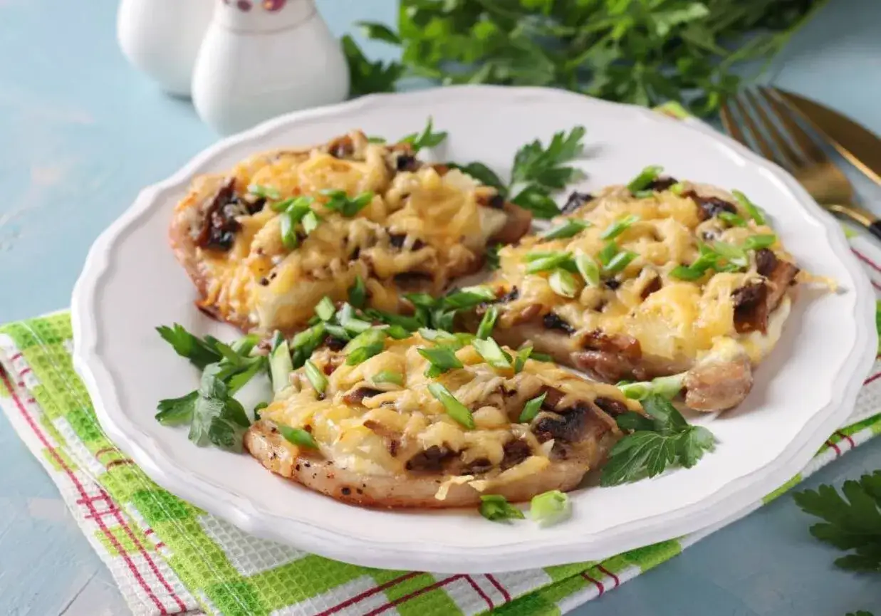 Schab w plastrach pieczony w piekarniku z pieczarkami i serem, posypany szczypiorkiem.