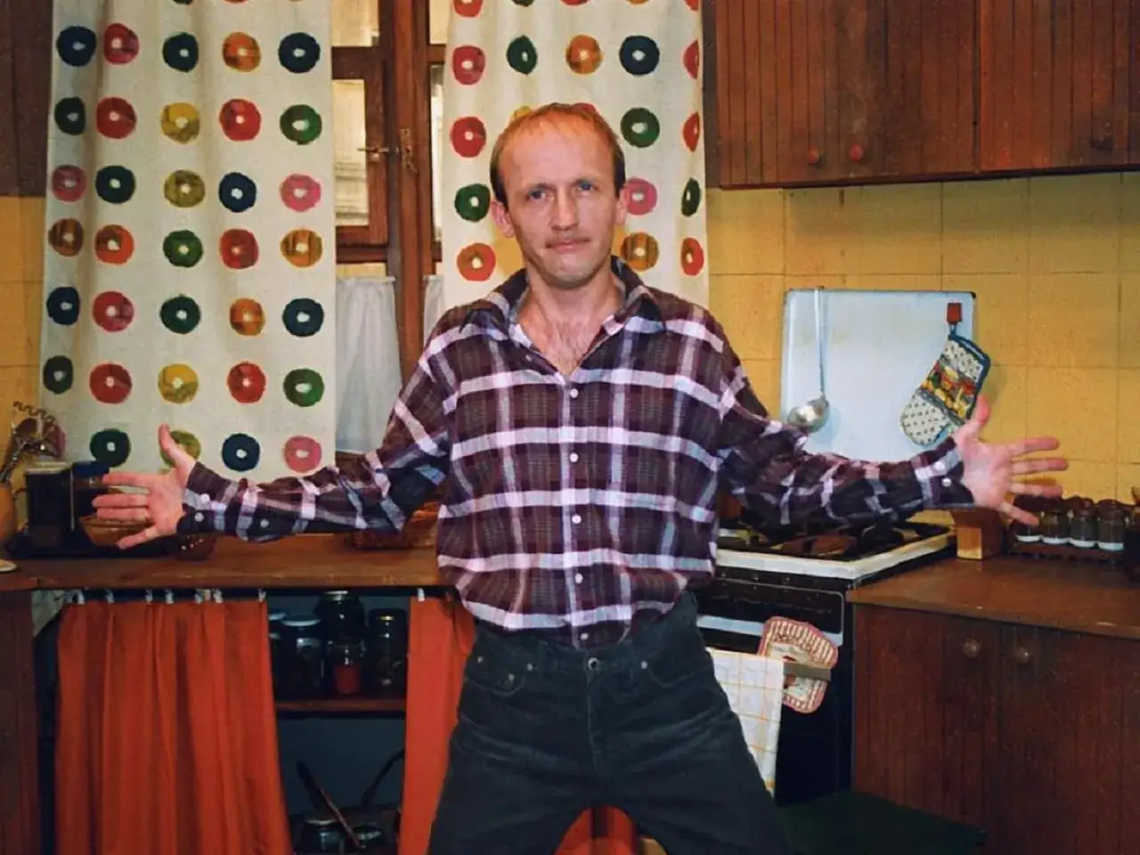 Tadeusz Norek w kratowanej koszuli stoi w kuchni z rękami rozłożonymi na boki.