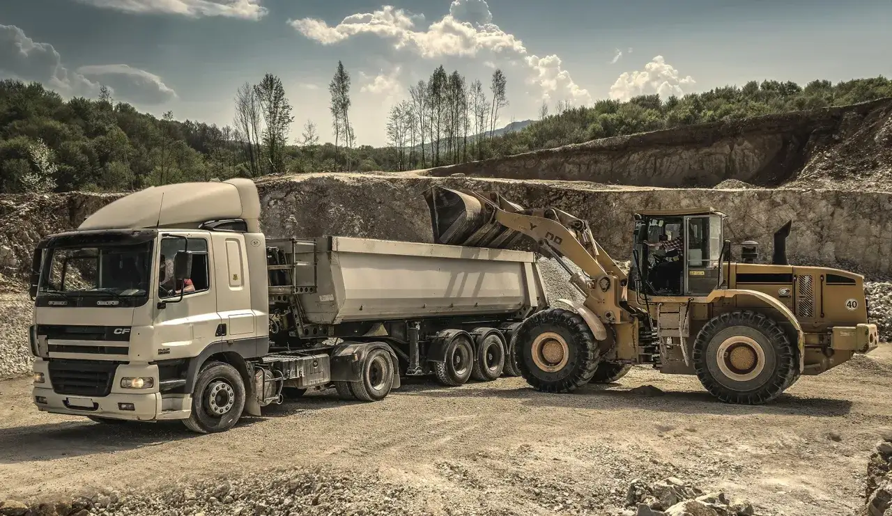 Ładowarka zasypuje kamieniem pod kostkę przyczepę ciężarówki na placu budowy.