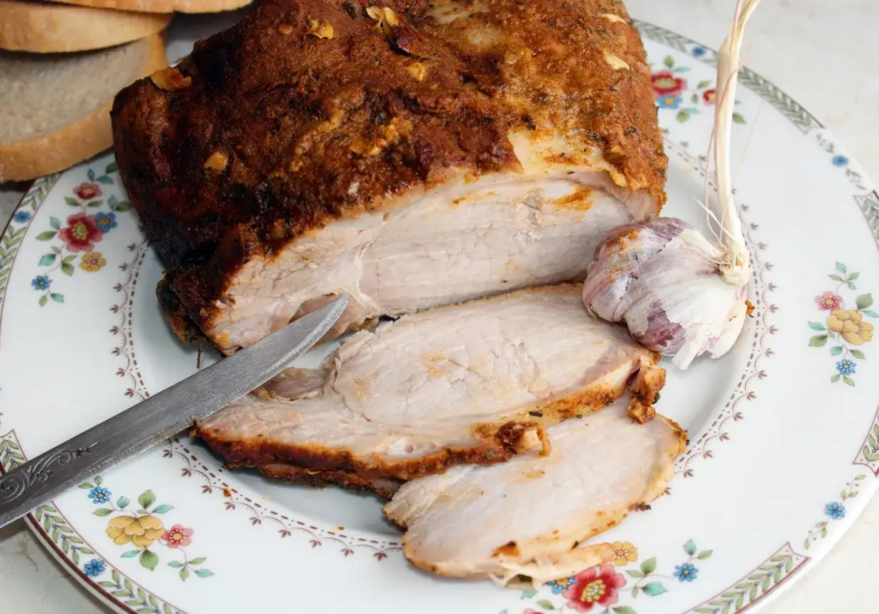 Soczysty schab pieczony w rękawie, pokrojony na talerzu z czosnkiem i chlebem. Ile czasu piec schab w rękawie żeby nie wyszedł wiór?