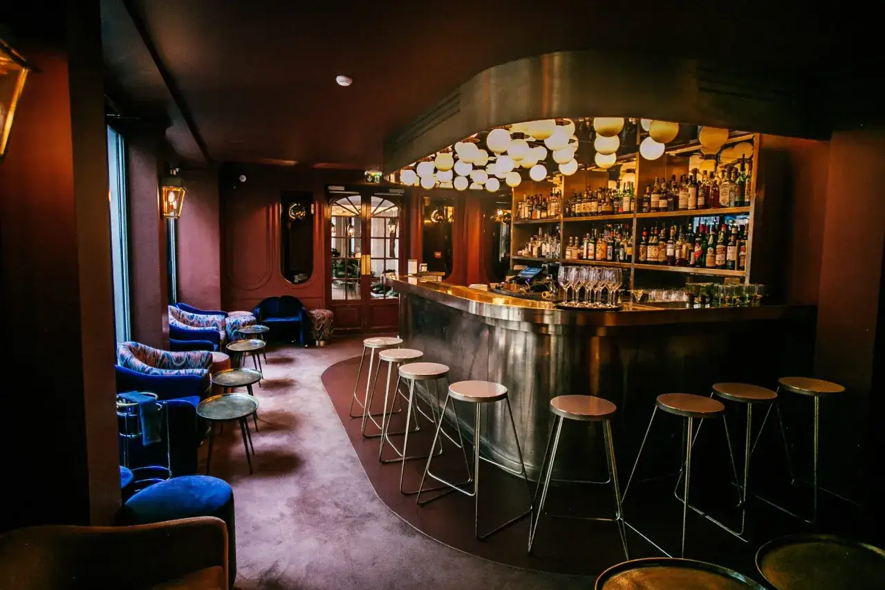 Elegancki bar w słynnym paryskim hotelu, z butelkami alkoholu na półkach i wygodnymi fotelami.