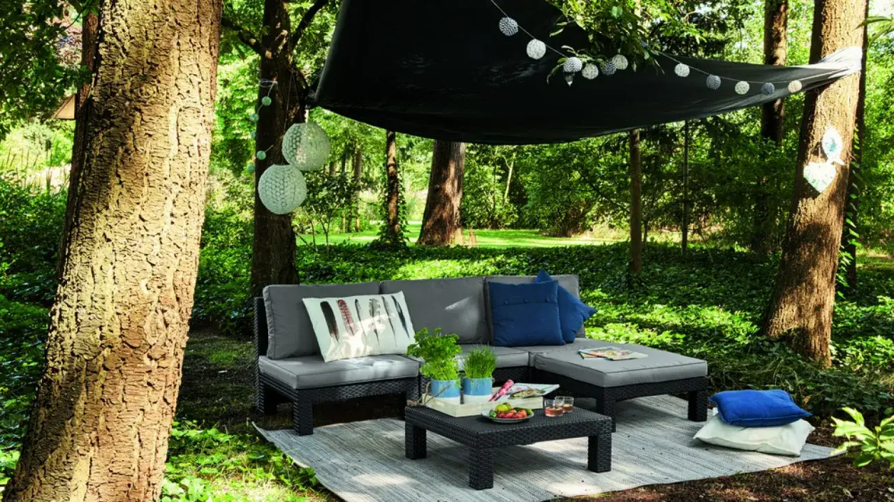 Idealna strefa relaksu w ogrodzie: wygodna sofa, stolik z owocami i ozdobne lampiony tworzą przytulne miejsce pośr&oacute;d zieleni.