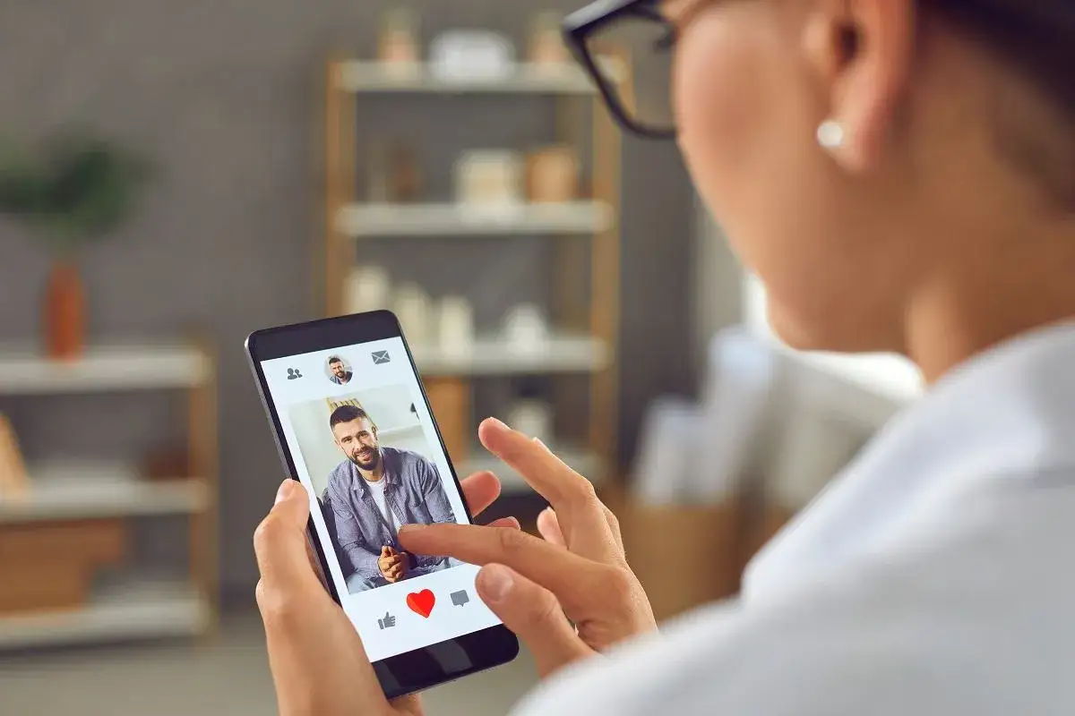 Kobieta przegląda profile na aplikacji do randkowania. Na ekranie telefonu widoczny jest uśmiechnięty mężczyzna.