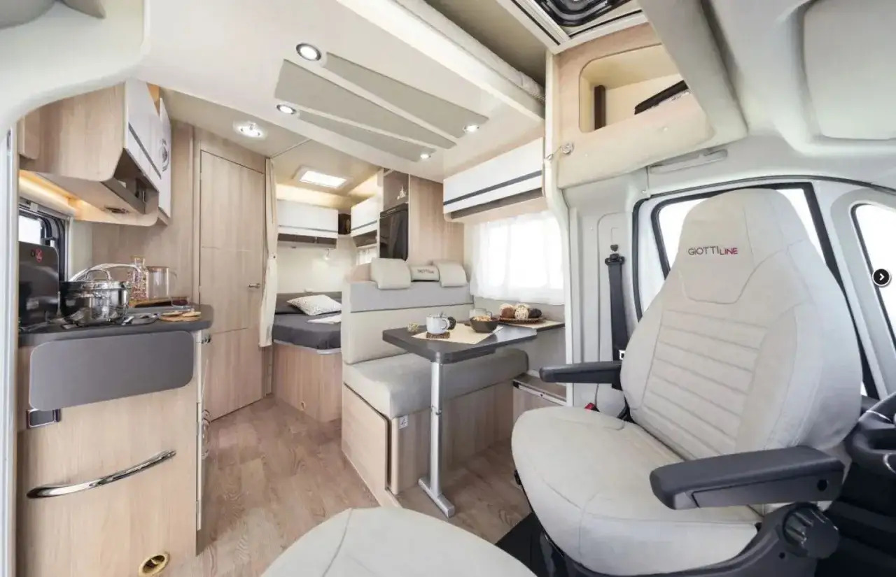 Wnętrze kampera 4 osobowego: aneks kuchenny, jadalnia, łóżko i wygodne fotele. Idealny na rodzinne wyjazdy.