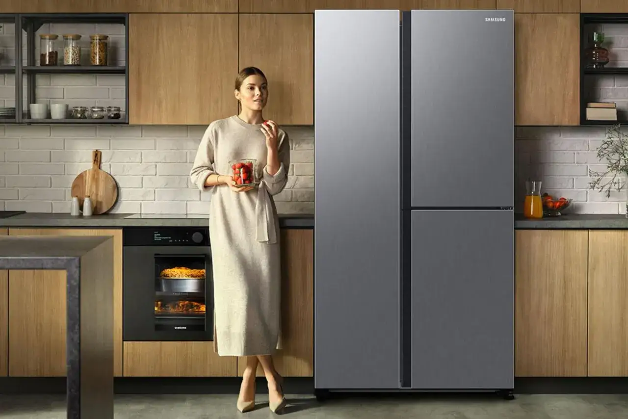 Kobieta w nowoczesnej kuchni z lodówką Samsung. Zastanawiasz się, jaką lodówkę wybrać? Ta elegancka, czterodrzwiowa lodówka Samsung to świetny wybór.
