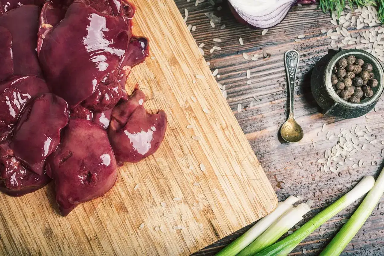 Świeża, surowa wątróbka drobiowa na desce, obok cebuli, przypraw i szczypiorku. Czy dzieci mogą jeść wątróbkę drobiową? Tak, to bogactwo witamin!