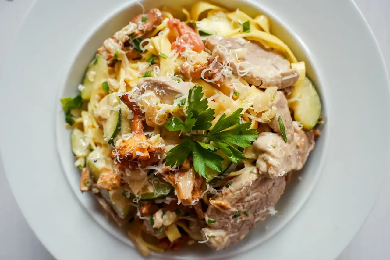 Pyszny makaron z polędwiczką, kurkami i cukinią, posypany parmezanem i udekorowany natką pietruszki.