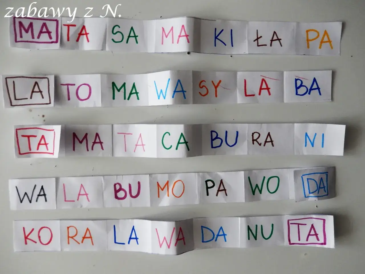 Zabawy z N. pomagają w nauce pisania i czytania. Na paskach papieru widać litery i sylaby: MATA, SA, MA, KI, ŁA, PA, LA, TO, MA, WA, SY, LA, BA, TA, MA, TA, CA, BU, RA, NI, WA, LA, BU, MO, PA, WO, DA, KO, RA, LA, WA, DA, NU, TA.
