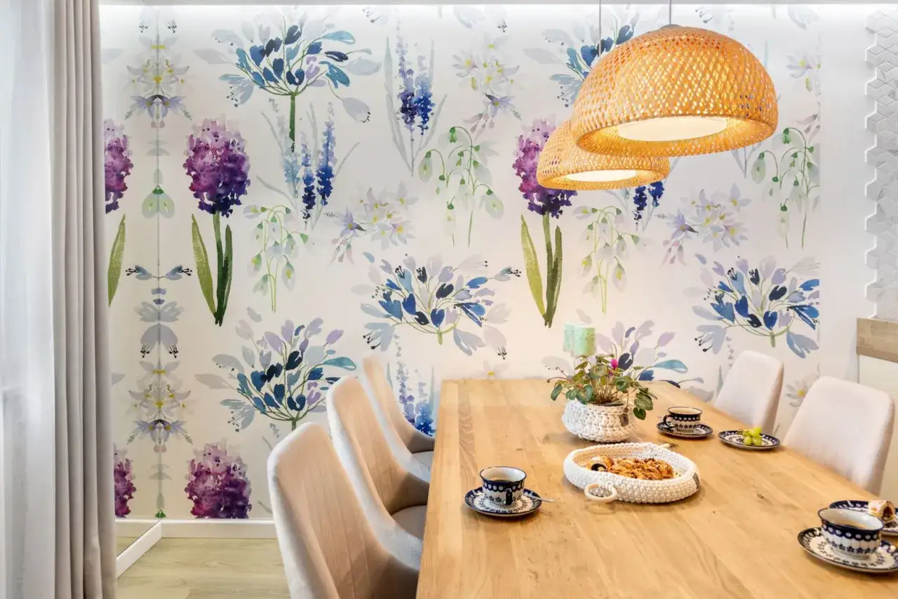 Kwiatowa tapeta na ścianę w kuchni przy stole i krzesłach dodaje uroku.