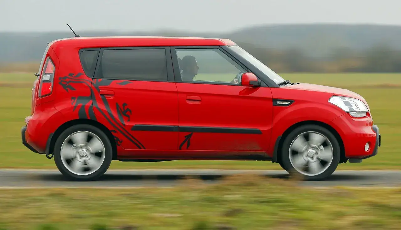 Czerwone Kia Soul z czarnym motywem smoka na boku jedzie po drodze.