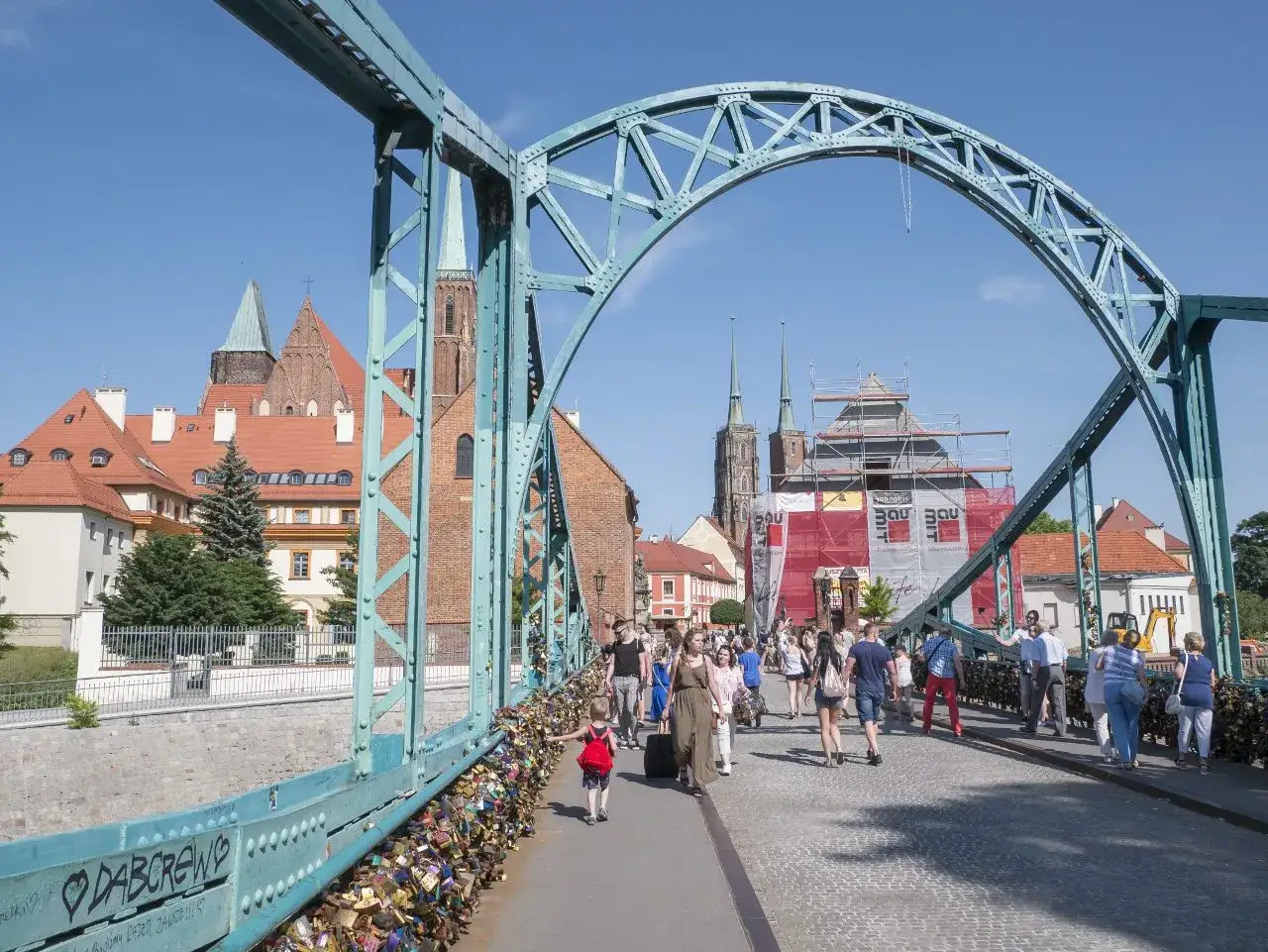 Most ludzi spaceruje po moście Tumskim we Wrocławiu, odkrywając darmowe atrakcje. W tle widać katedrę i Ostr&oacute;w Tumski.