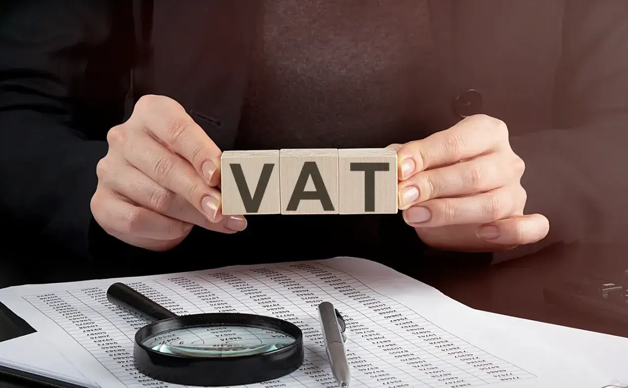 Ręce trzymają kostki z napisem VAT, symbolizujące rozliczenia podatkowe w PKD handlu samochodami.