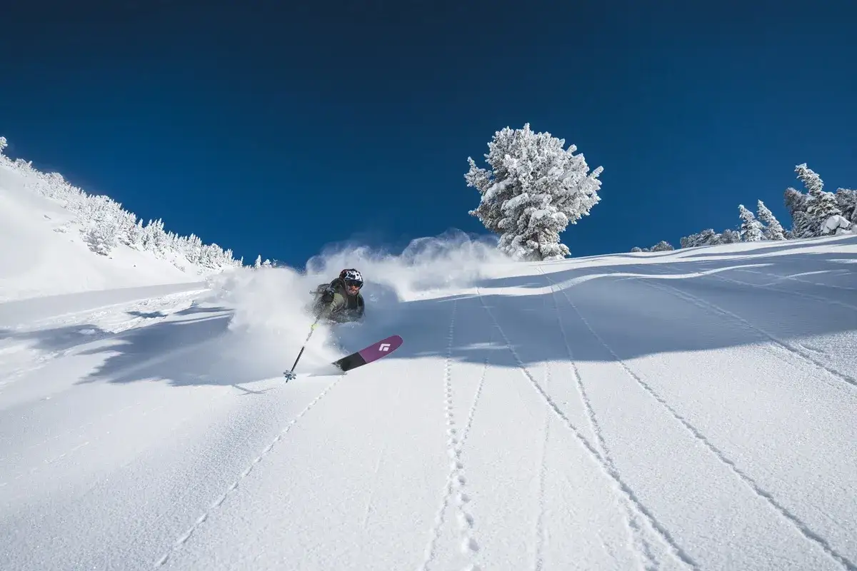 Narciarz w akcji, tworzący chmurę śniegu podczas zjazdu. To esencja ski alpinizmu.