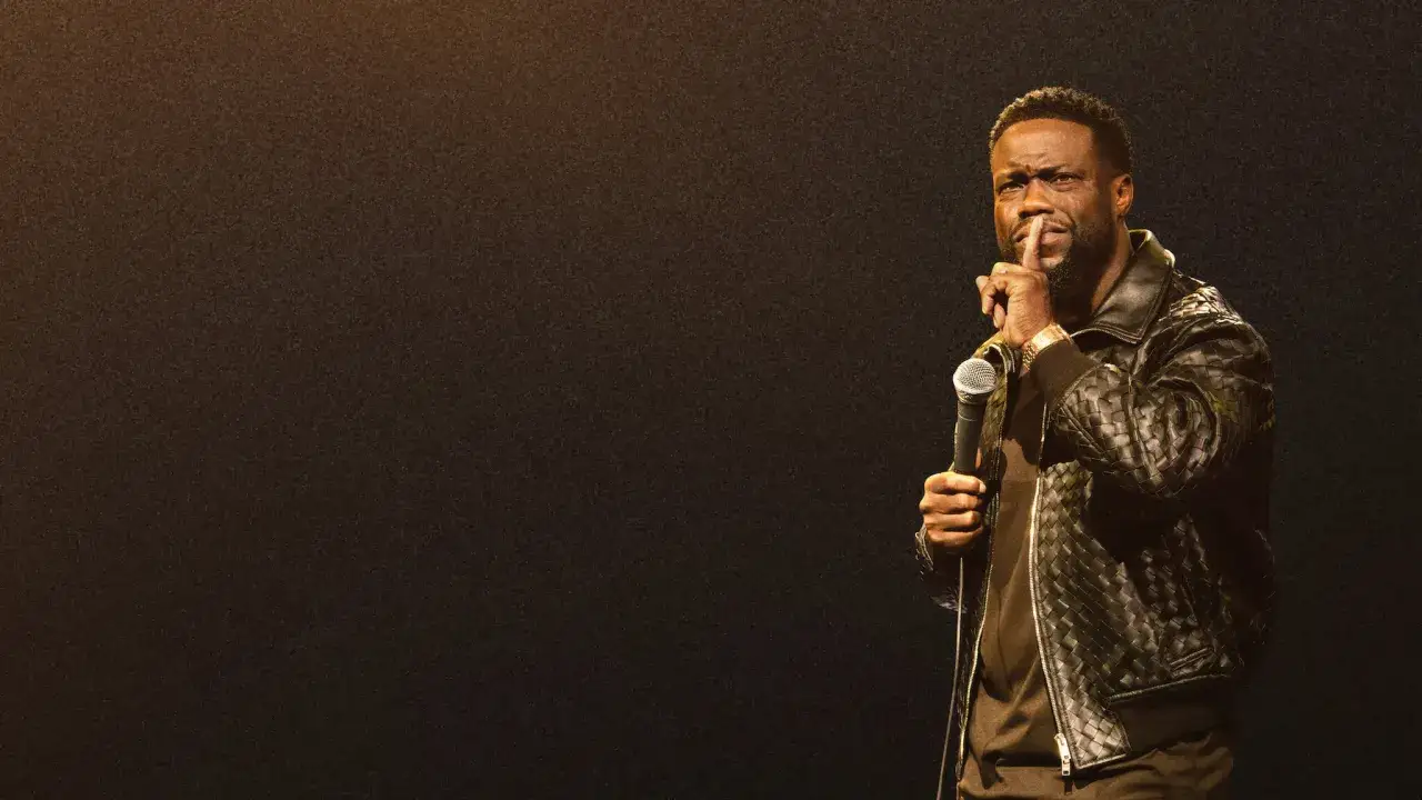 Kevin Hart stand up, trzymając mikrofon i gestykulując do publiczności.