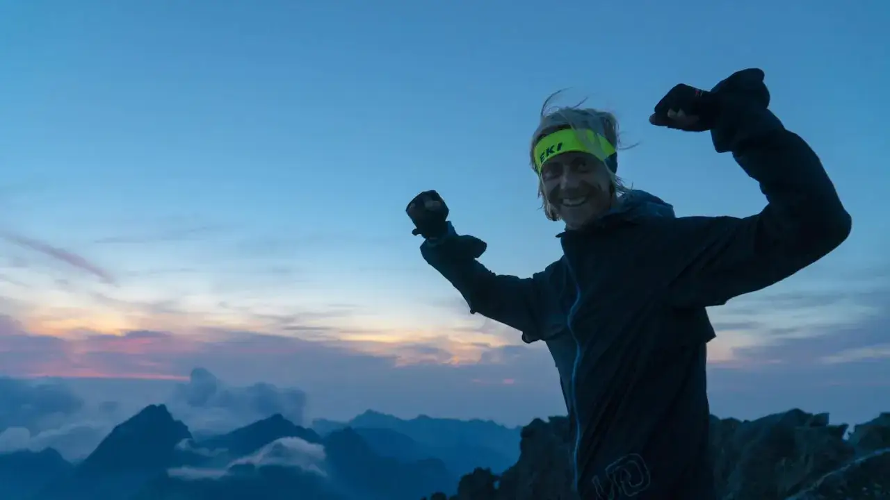 Uśmiechnięty Roman Ficek na szczycie g&oacute;rskim o wschodzie słońca, zaciśnięte pięści w geście triumfu.