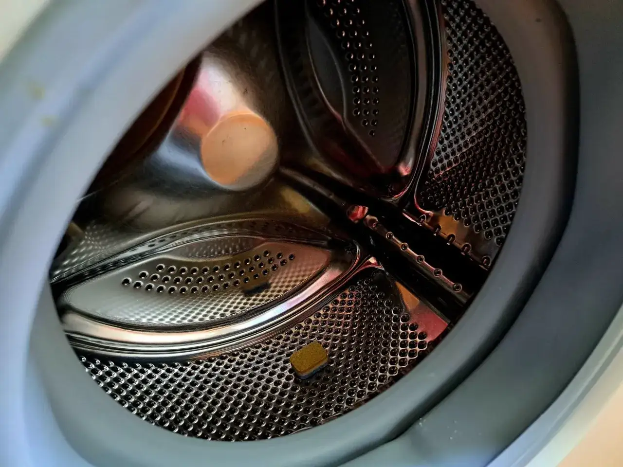 Bęben pralki po czyszczeniu tabletkami do zmywarki. Widać metalowe elementy i otwory, a także resztki tabletki.