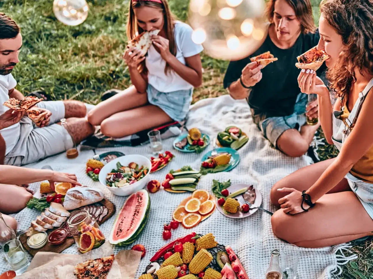 Przyjaciele cieszą się pysznym przyjęciem w ogrodzie, jedząc pizzę i świeże owoce.