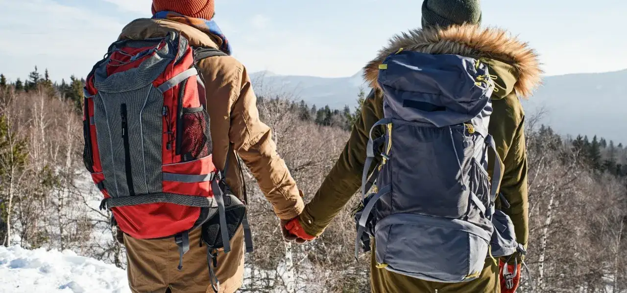 Para zimą w góry, z plecakami i ciepło ubrani, trzymają się za ręce. Wiedzą, co zabrać w góry zimą.