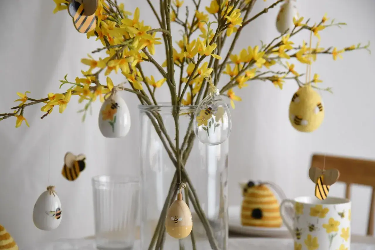 Wielkanocne kwiaty forsycji ozdobione zawieszkami w kształcie jajek i pszcz&oacute;ł.