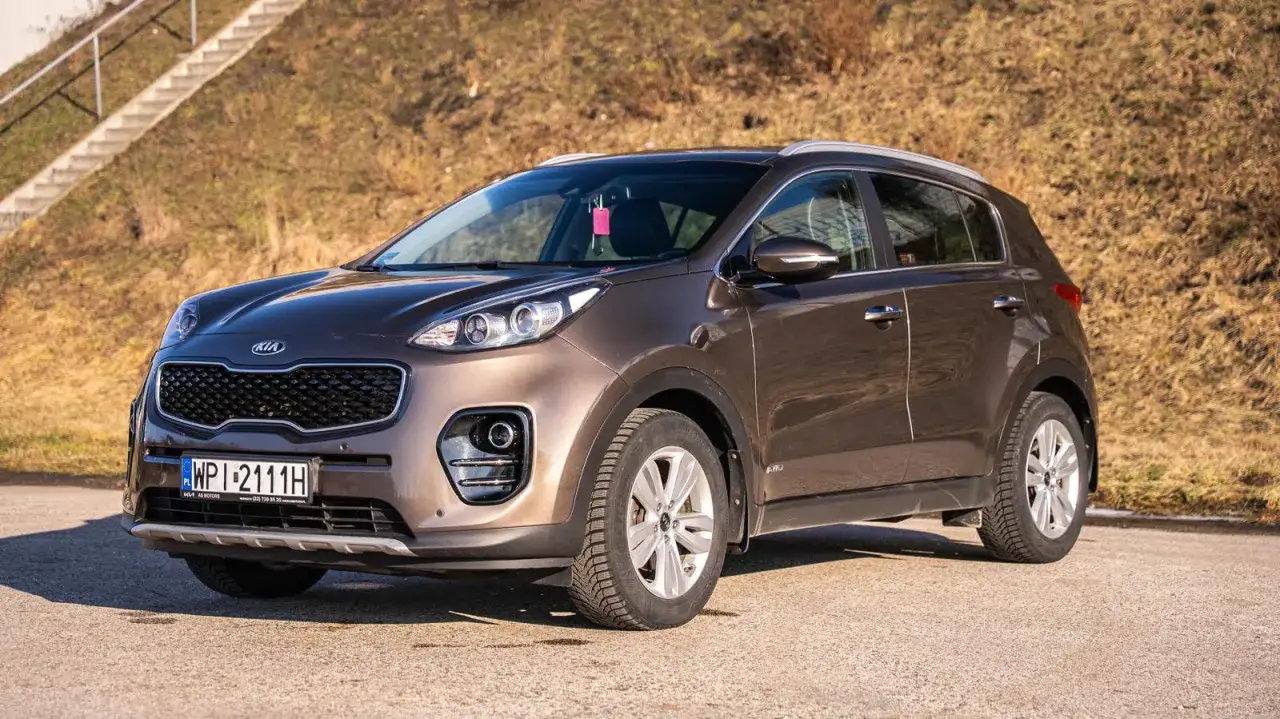 Brązowy Kia Sportage z silnikiem 1.7 CRDi, czy jest dobry? Ten SUV stoi na tle suchej trawy i schodów.