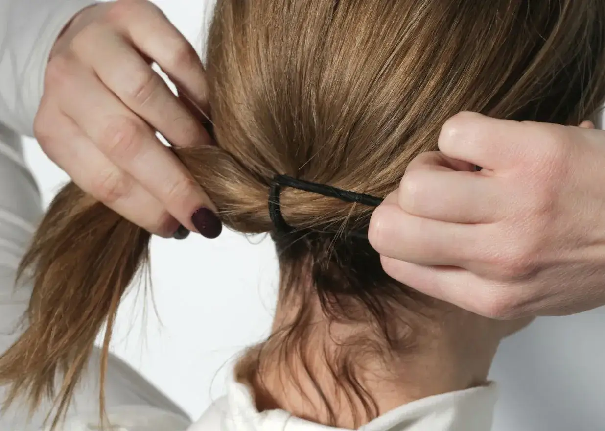 Dłonie zaciskają czarne frotki do włosów na końskim ogonie.