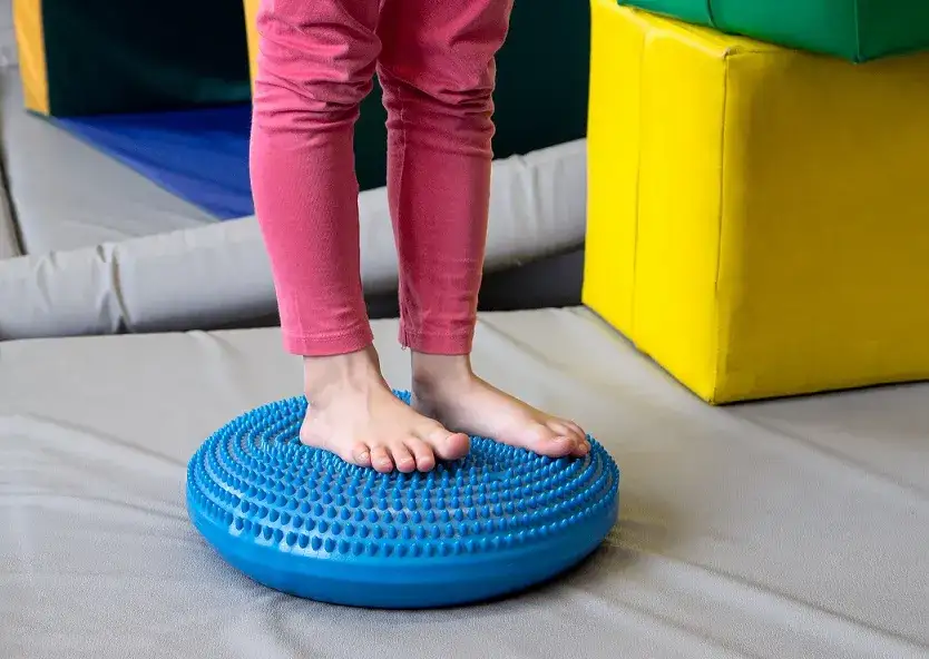 dziecko ćwiczy r&oacute;wnowagę na dysku sensorycznym