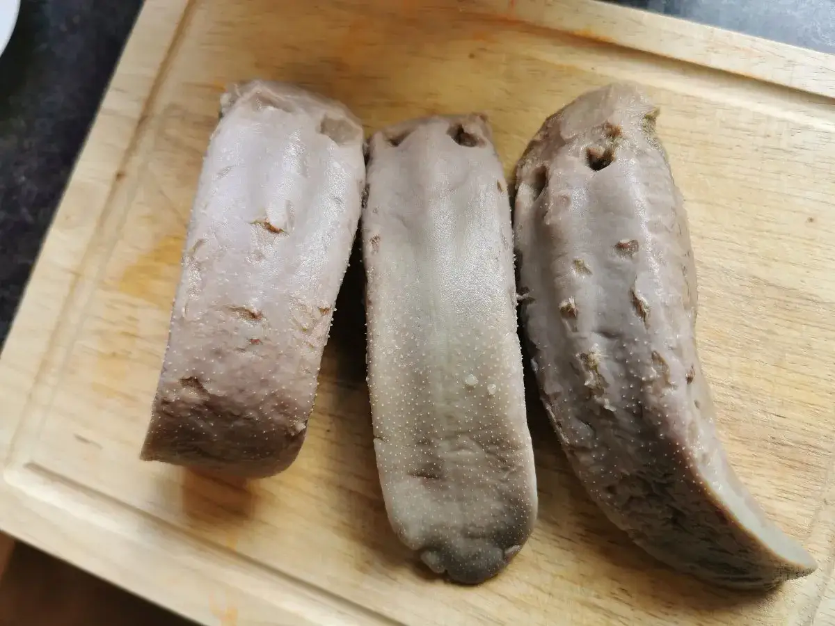 Trzy ugotowane ozory wieprzowe na desce. Zobacz, jak zdjąć skórę z ozora wieprzowego, aby przygotować pyszne danie.