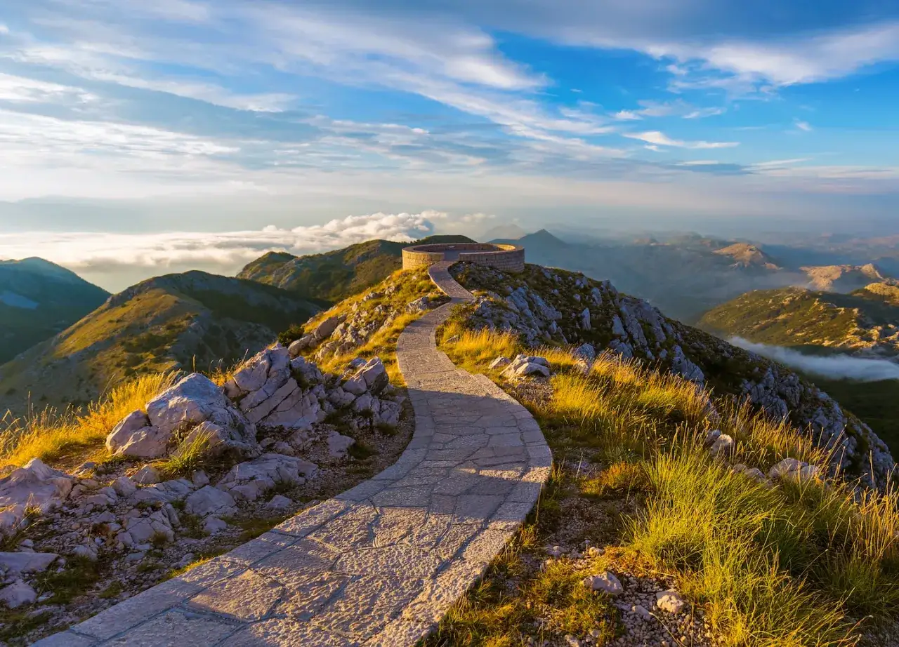 Kamienna ścieżka prowadzi do okrągłego punktu widokowego na szczycie góry. Wspaniały widok na pasma górskie i chmury, idealny na podróż do Czarnogóry we wrześniu.