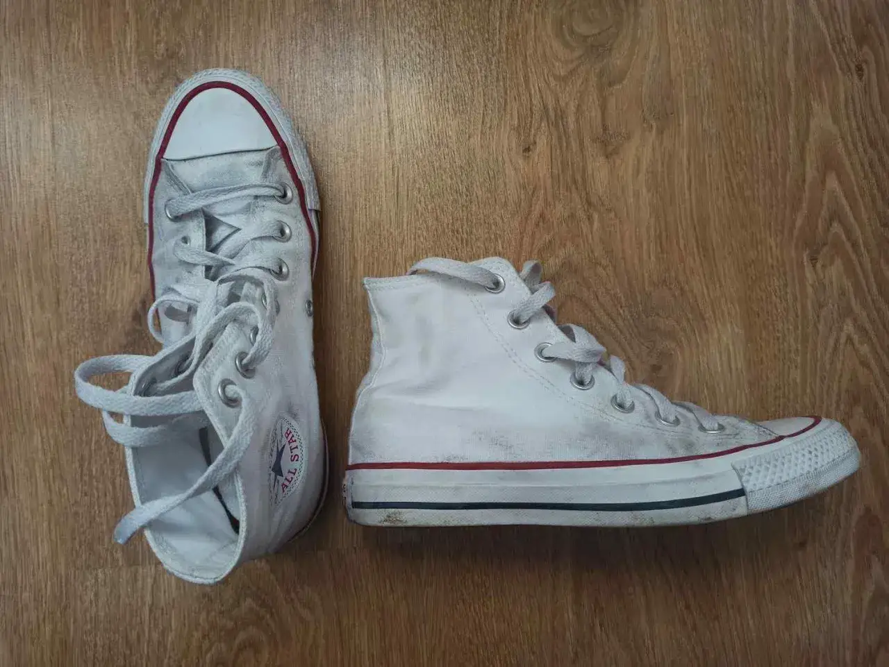 Białe trampki Converse na drewnianym tle. Czas je wyczyścić, oto jak prać Conversy w pralce, by znów były jak nowe.