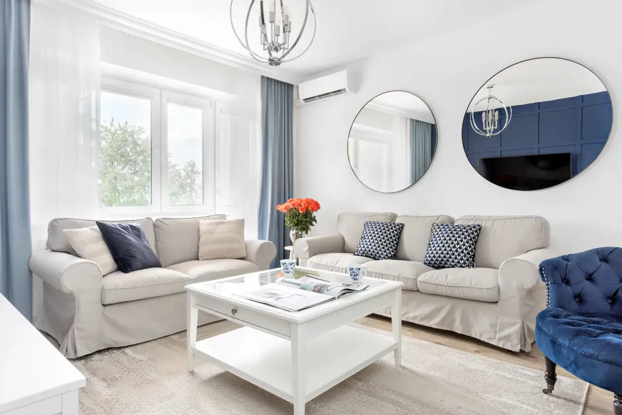 Elegancka aranżacja ściany za kanapą: dwa okrągłe lustra i granatowa, panelowa ściana dodają głębi.