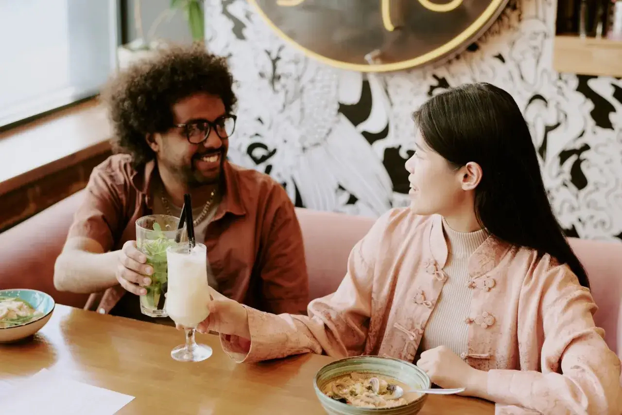 Udany początek randki z Tindera. Uśmiechnięta para wznosi toasty drinkami w restauracji.