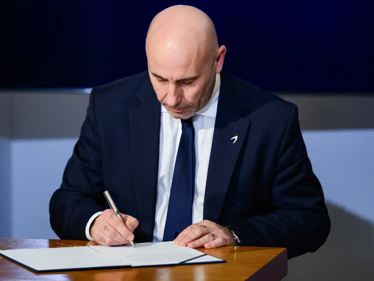 Mężczyzna w garniturze podpisuje dokument, co może oznaczać rezygnację ze stanowiska kierowniczego.