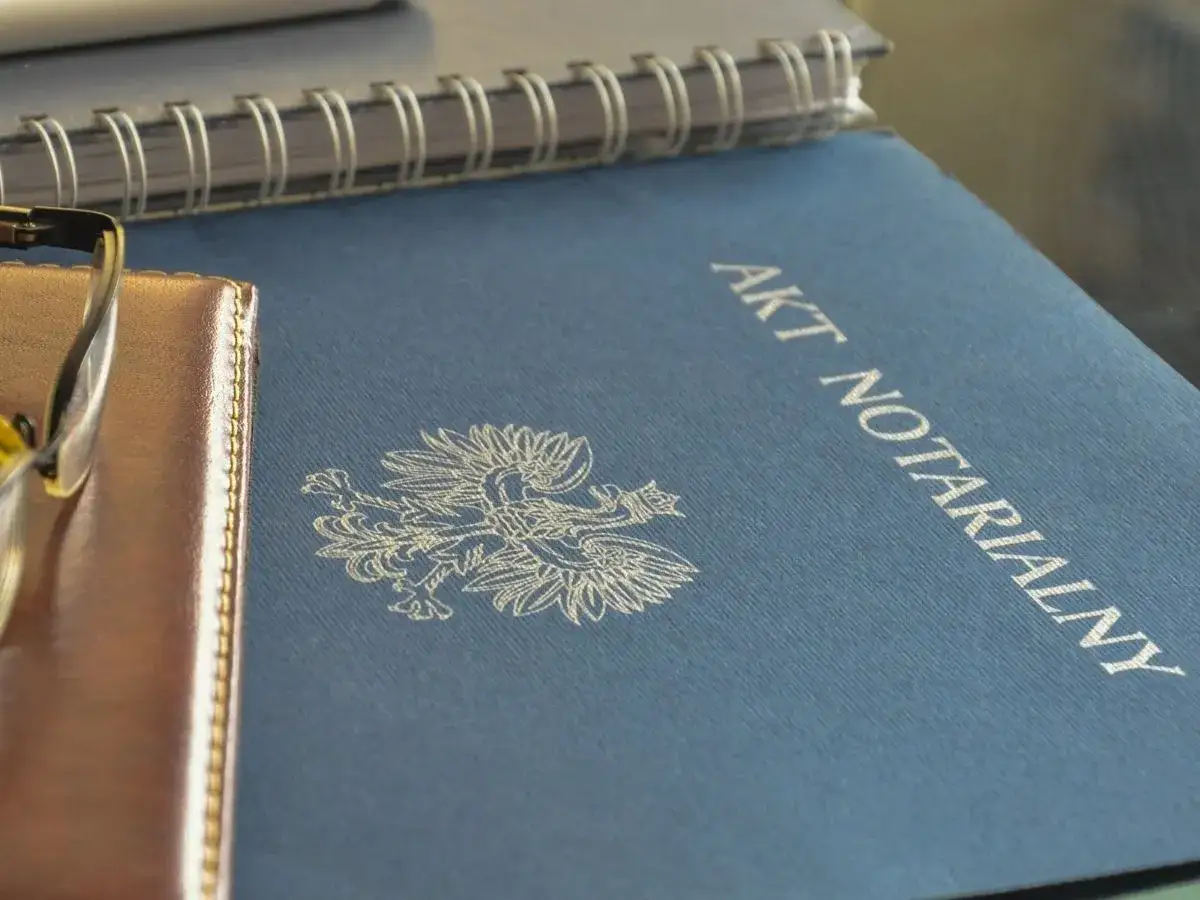 Akt notarialny, symbol polskiego orła i okulary na brązowej okładce. Czy akt notarialny jest aktem własności?