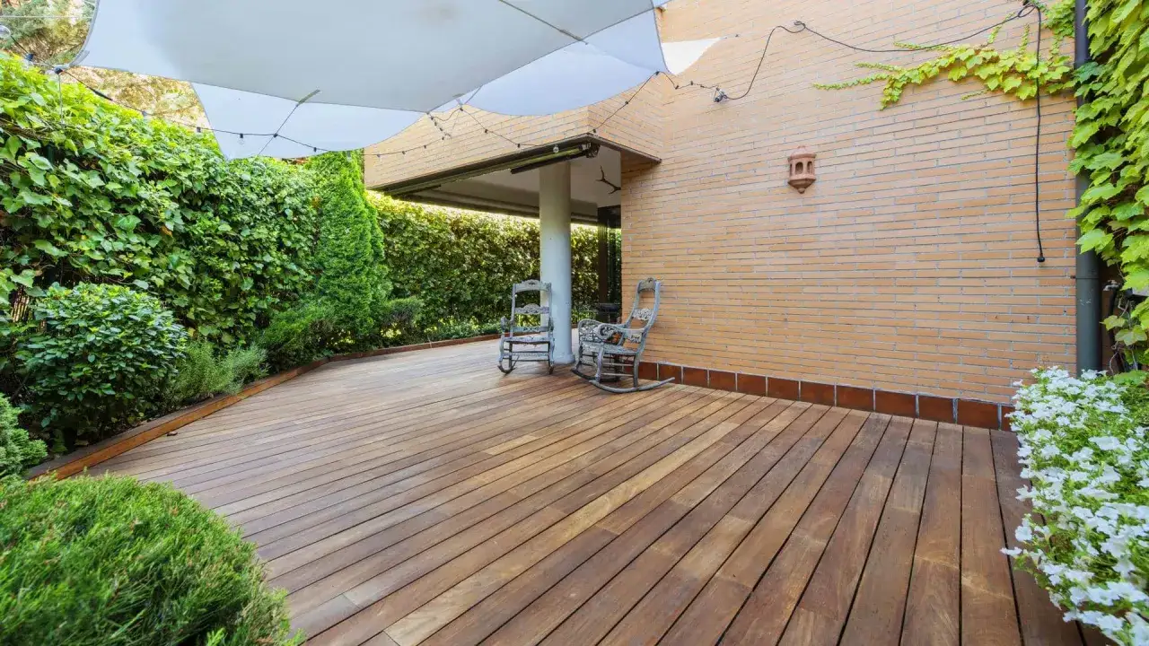 Drewniany taras, otoczony zielenią, z dwoma fotelami bujanymi. Idealne miejsce na relaks, pokazujące, czym wyłożyć taras tanio i efektownie.