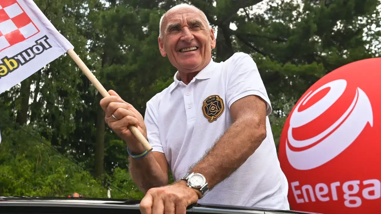 Uśmiechnięty mężczyzna trzyma flagę. Co się stało Langowi? Wygląda na szczęśliwego, może właśnie wygrał wyścig.