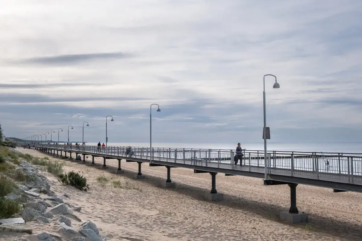 Długie molo nad Bałtykiem, z ludźmi spacerującymi i podziwiającymi widoki. Czy to miasto Mielno?