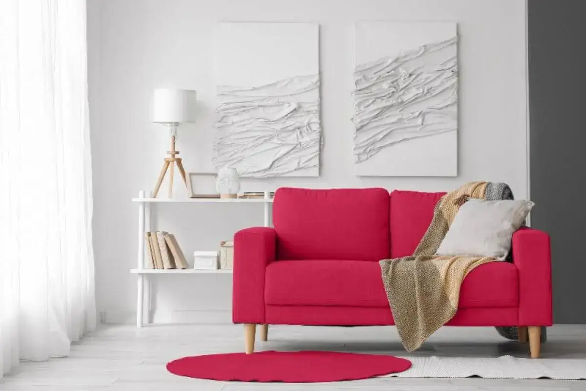 Jasny salon z czerwoną kanapą, białymi obrazami na ścianie i białym dywanem.