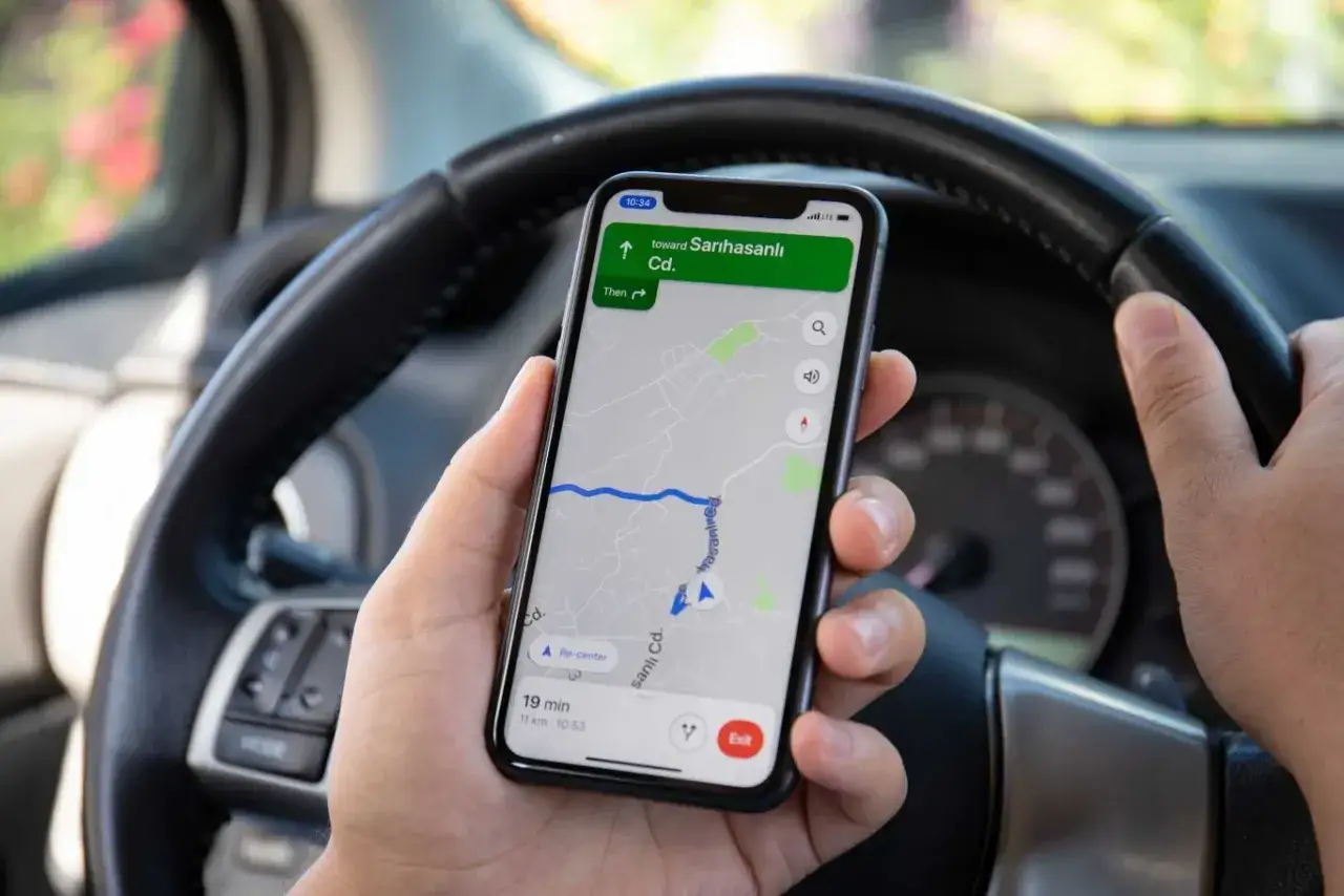 Ręce kierowcy trzymają telefon z nawigacją, co stanowi niebezpieczne korzystanie z telefonu podczas jazdy.