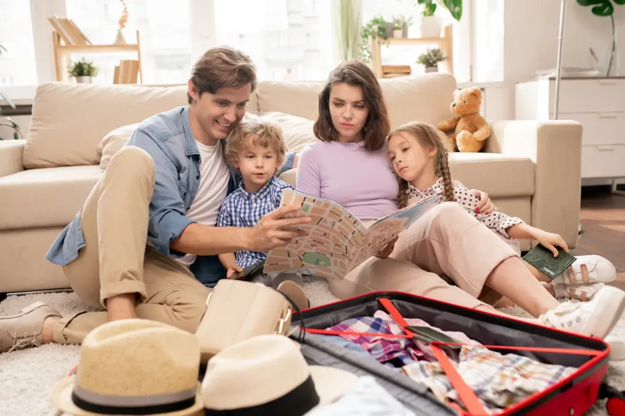 Rodzina planuje, gdzie na wakacje z niemowlakiem, przeglądając mapę. Walizka już spakowana, czeka na podróż.