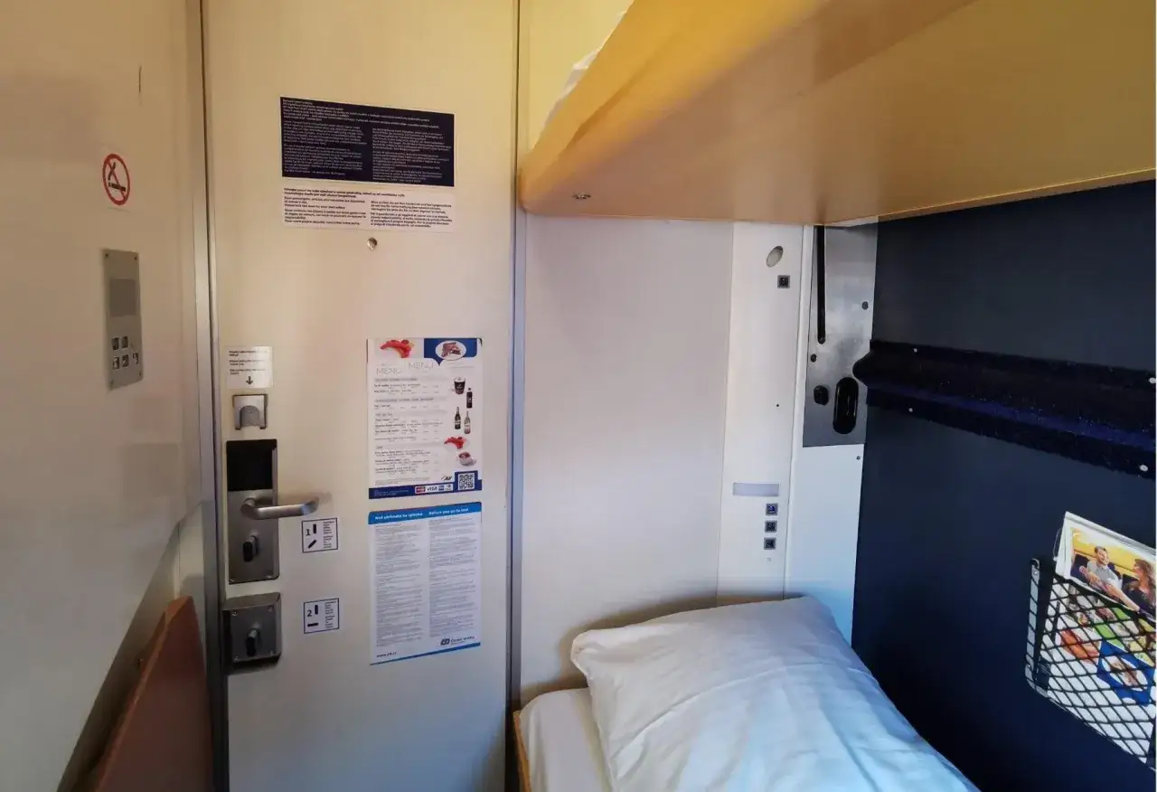 Wnętrze przedziału sypialnego w pociągu do Budapesztu. Widok na łóżko, drzwi z menu i instrukcjami.