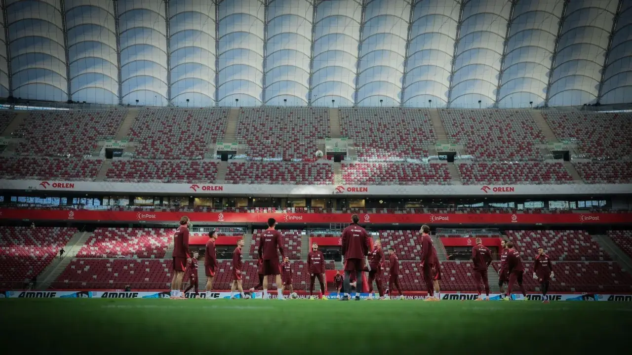 Piłkarze na murawie stadionu, który pomieści 58 000 widzów. Widok na puste trybuny i dach.
