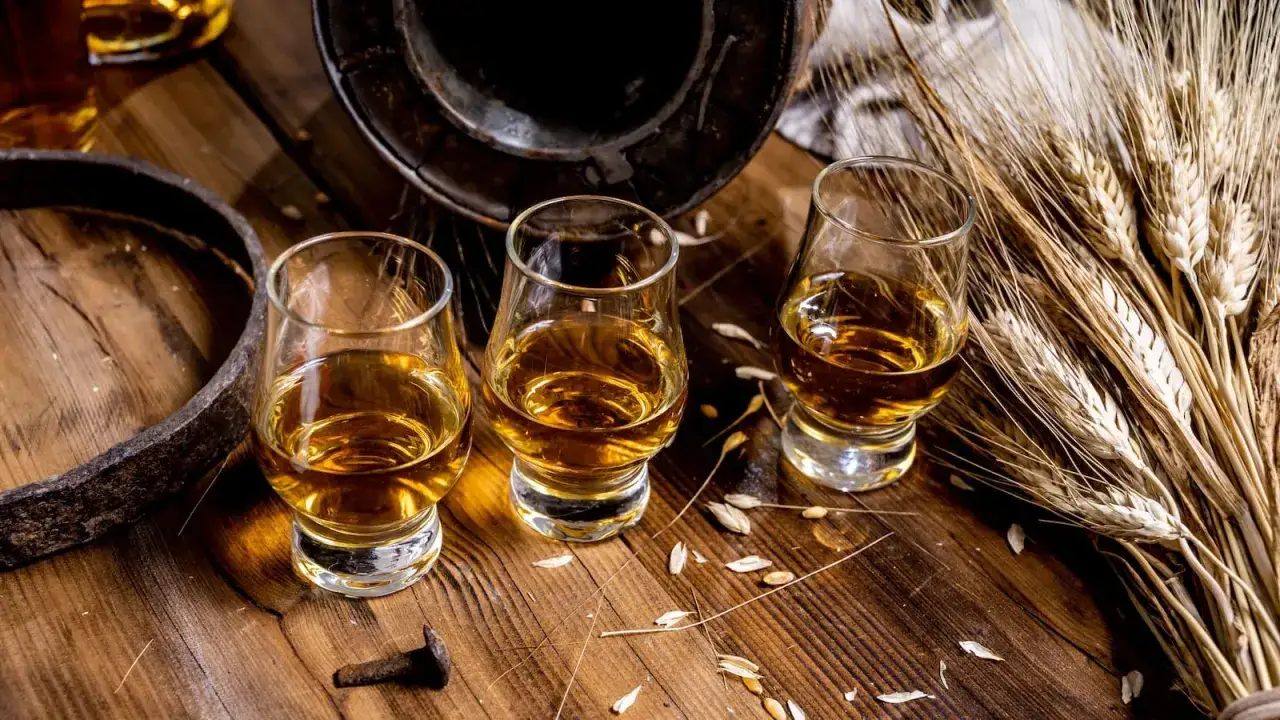 Trzy kieliszki bursztynowego trunku, kłosy zbóż i fragment beczki. Degustacja ancnoc 12.