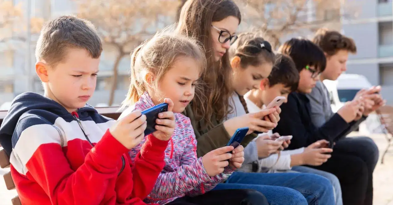 Dzieci siedzą na ławce, pochłonięte grami dla 4 latka na telefon.