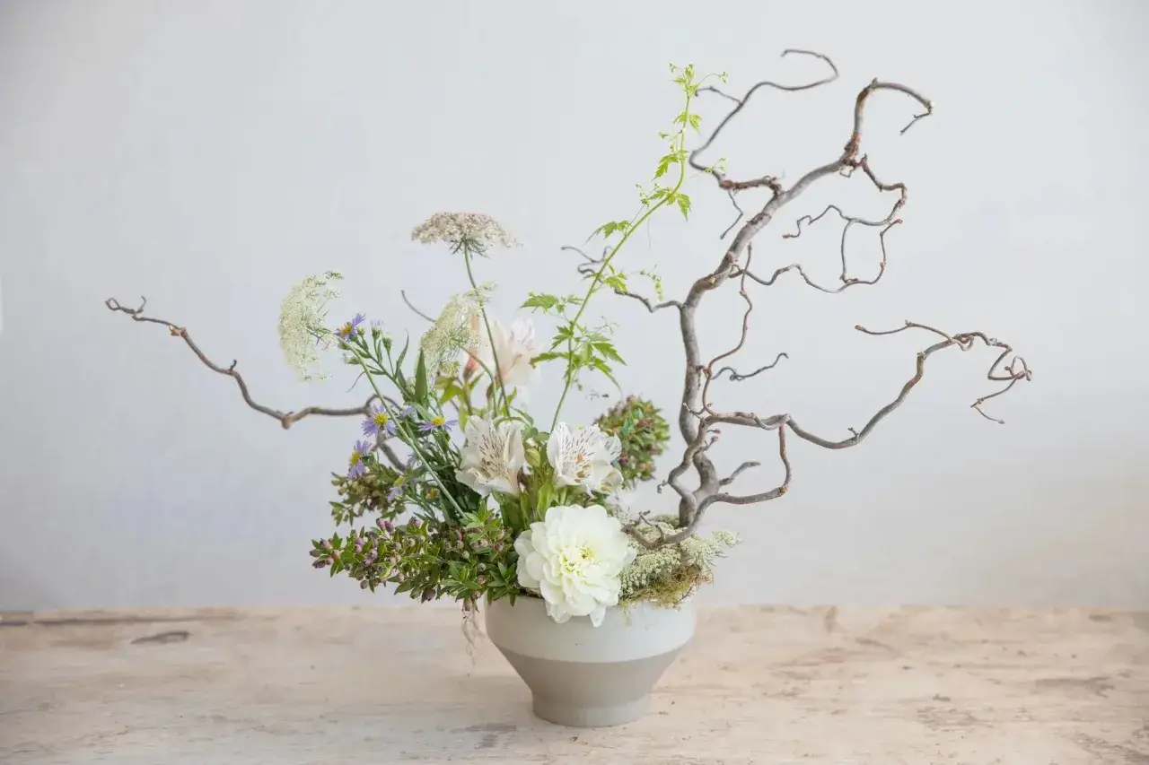 Inspiracja ikebana jak zrobić: delikatne kwiaty, gałązki i mech w szarej wazonie.