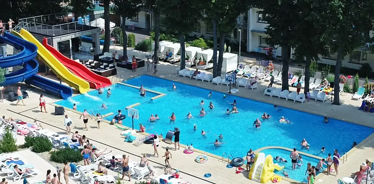 Ośrodek wypoczynkowy Jantar tętni życiem: dzieci zjeżdżają ze zjeżdżalni, dorośli kąpią się w basenie, inni relaksują się na leżakach.