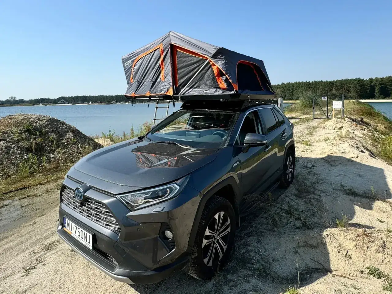 Szara Toyota RAV4 z namiotem dachowym nad jeziorem. Idealna na wakacje, może być dostępna w ramach cesja leasingu toyota.
